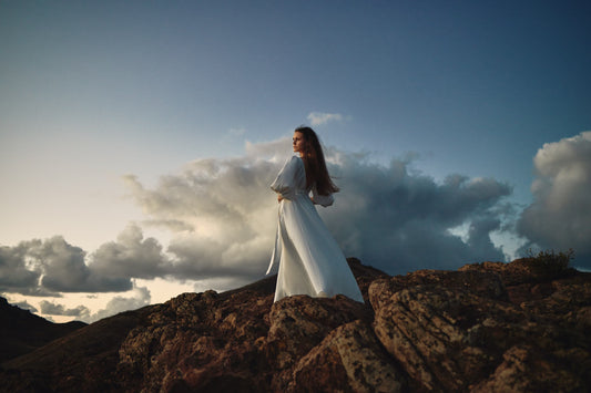 Silhouette of a person standing on a rocky peak at sunset, embodying strength and grace, in a photograph by Celin May.