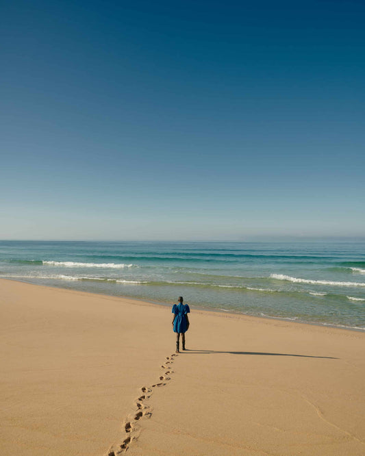The artpiece 'Encounter' by Andreas Ortner from the series Aqua shows a woman on the beach with footprints behind her in the sand while walking towards the sea.