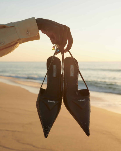 The artpiece 'Release' by Andreas Ortner from the series Aqua shows a hand holding two black shoes with a beach and sea in the background