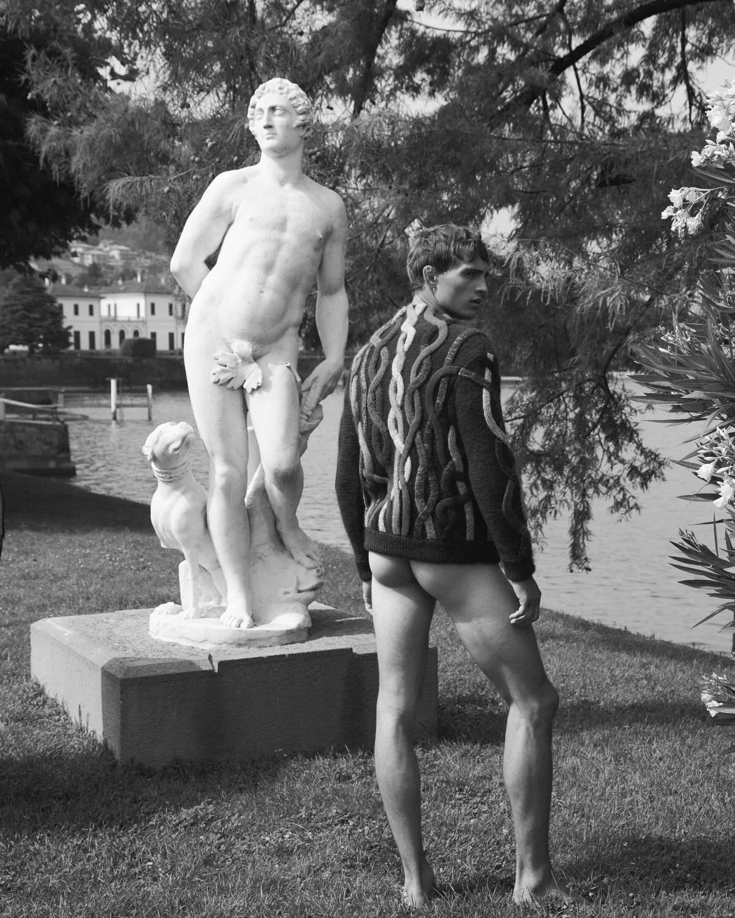 The artpiece 'Intimate' by Andreas Ortner shows a man from the back wearing a sweater and no bottoms standing diagonally in front of a greek statue of a naked man. 