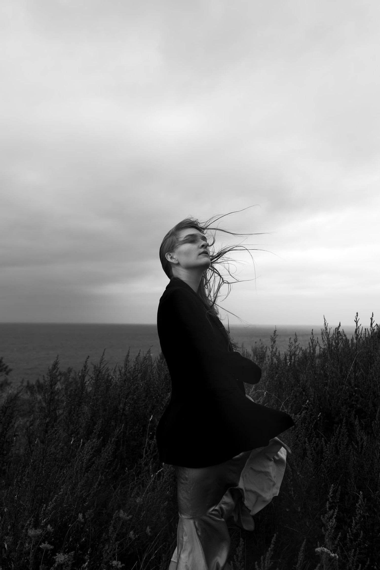 Person standing in the wind, embodying chaos and dreams, in a black and white photograph by Celin May from "The Unknown" collection.
