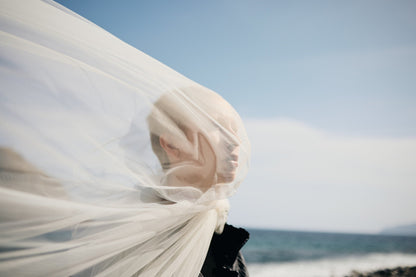 Model's face obscured by a transparent veil, suggesting a gust of wind, in a sunlit photograph by Celin May.