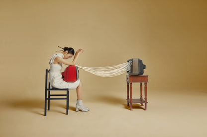 The artpiece 'Connect' by Hui Long shows a woman trying with a red old CRT tv on her lap, which is connected to another CRT TV standing on a side table by a bunch of cables.