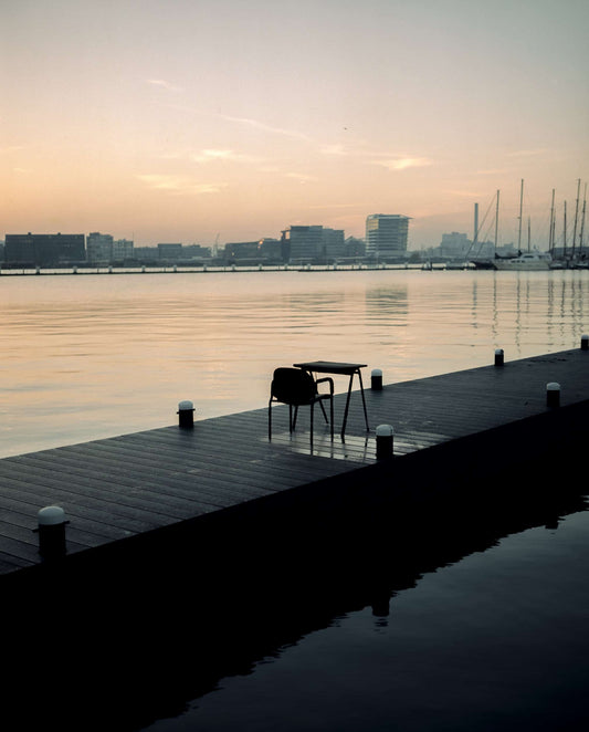 The artpiece 'Amsterdam Noord #1' by Jildo Tim Hof which shows a lonely table and chair sitting on a pier next to the water in Amsterdam-Noord, The Netherlands