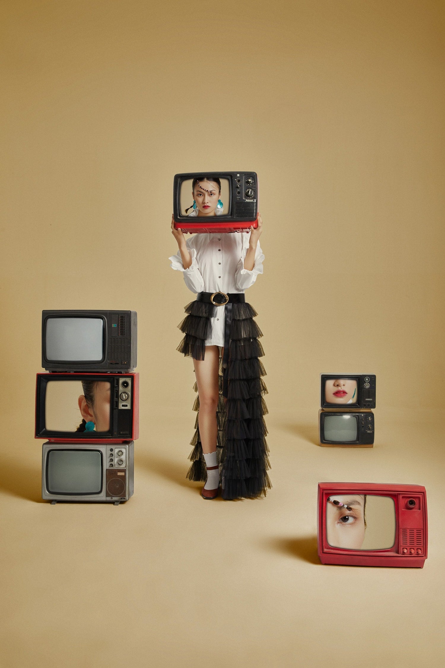 The artpiece 'Lost' by Hui Long shows an unreal scene with a woman holding up a tv while surrounded by several television sets. Her face is hidden in reality, while the TVs show ports of a womans face.