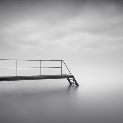 The artpiece 'Eternity of Silence' by Marco Maljaars shows a catwalk and staircase leading into silent waters. Shot in black and white.