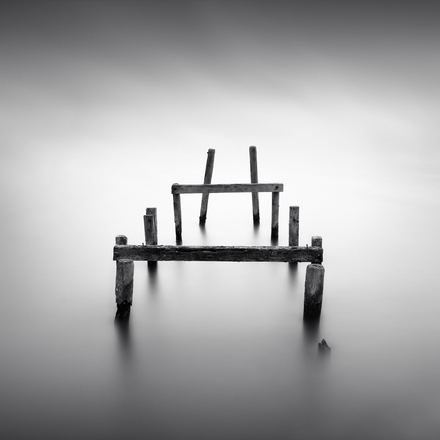 The artpiece 'Fallen Apart' by Marco Maljaars shows the remains of a pier sitting lonely on a silent lake. Shot in black and white.