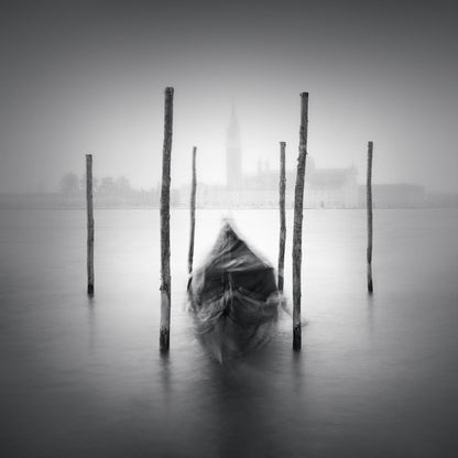 The artpiece 'Gondola' by Marco Maljaars shows a long exposure black and white image of a single gondola in Venice, with the iconic city visible in the background.