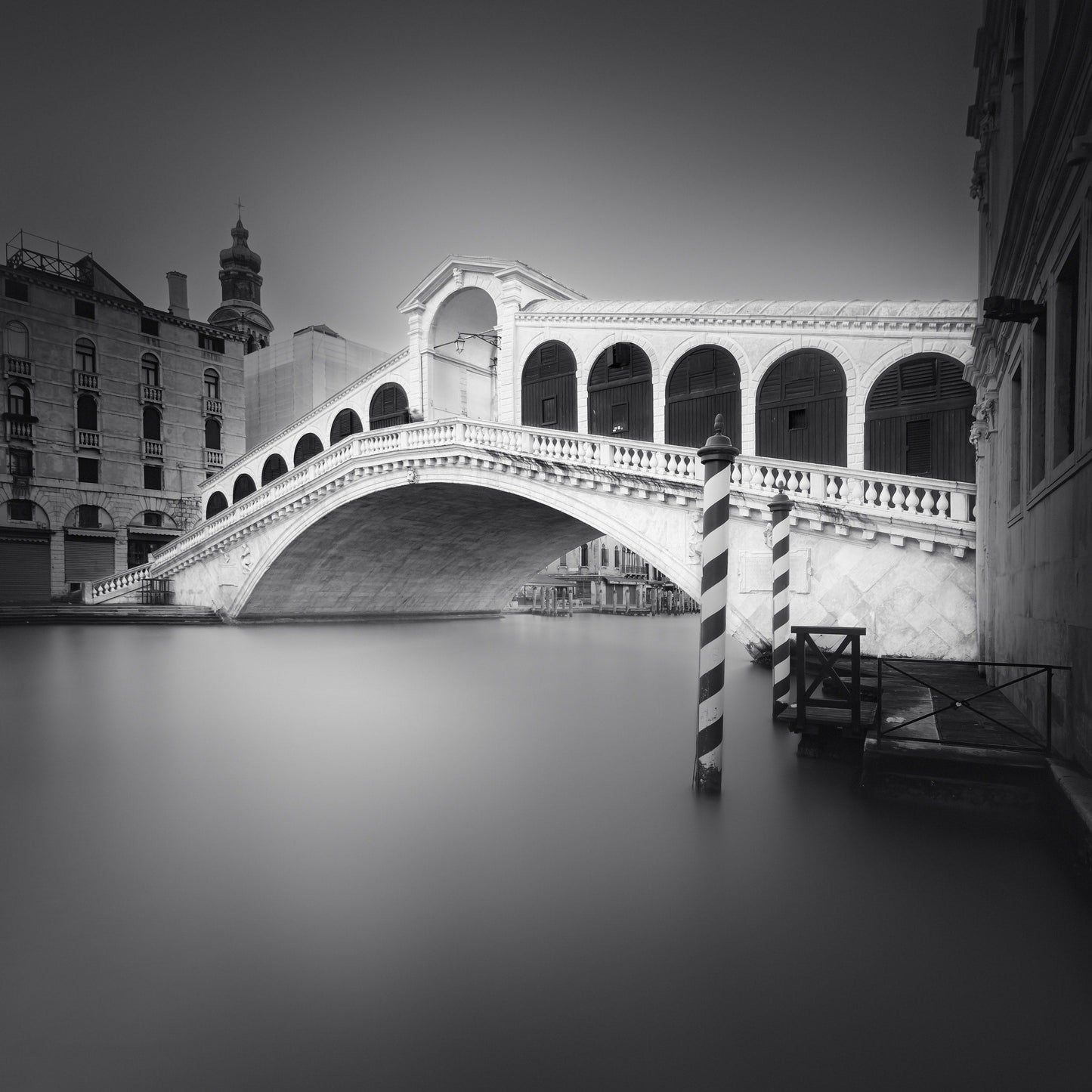 The artpiece 'Ponte di Rialto' by Marco Maljaars shows the famous bridge in Venice with serene quiet waters underneath in a beautiful black and white image.