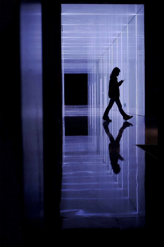 The artpiece 'Surreal World' by Michael Cai shows a person walking in a hallway that is lit up in a purple light, giving the image a surreal feeling.