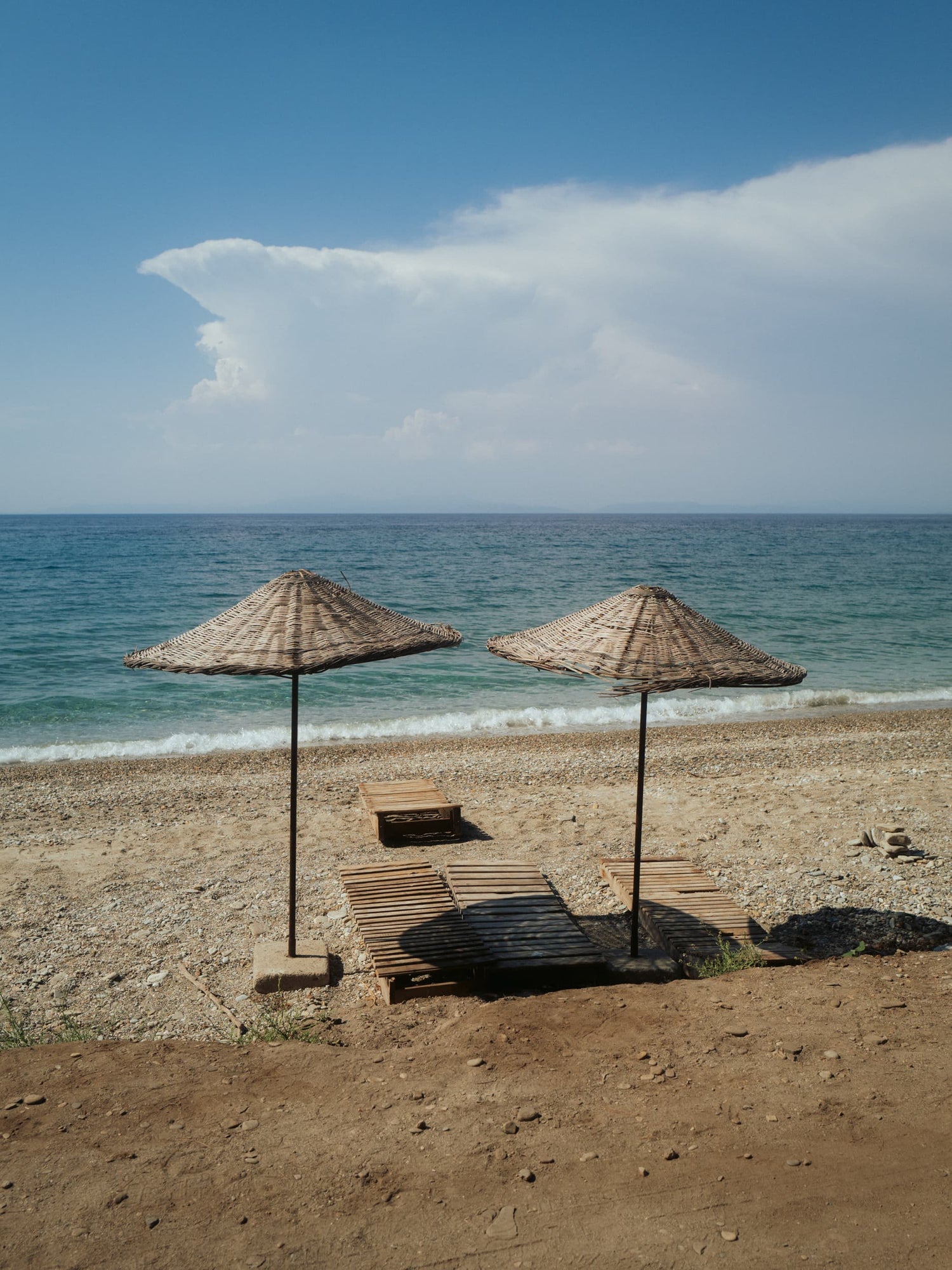 The artpiece 'Deniz' by Mikail Sahin showing two parasols on a tranquil beach next to 2 beachbeds.
