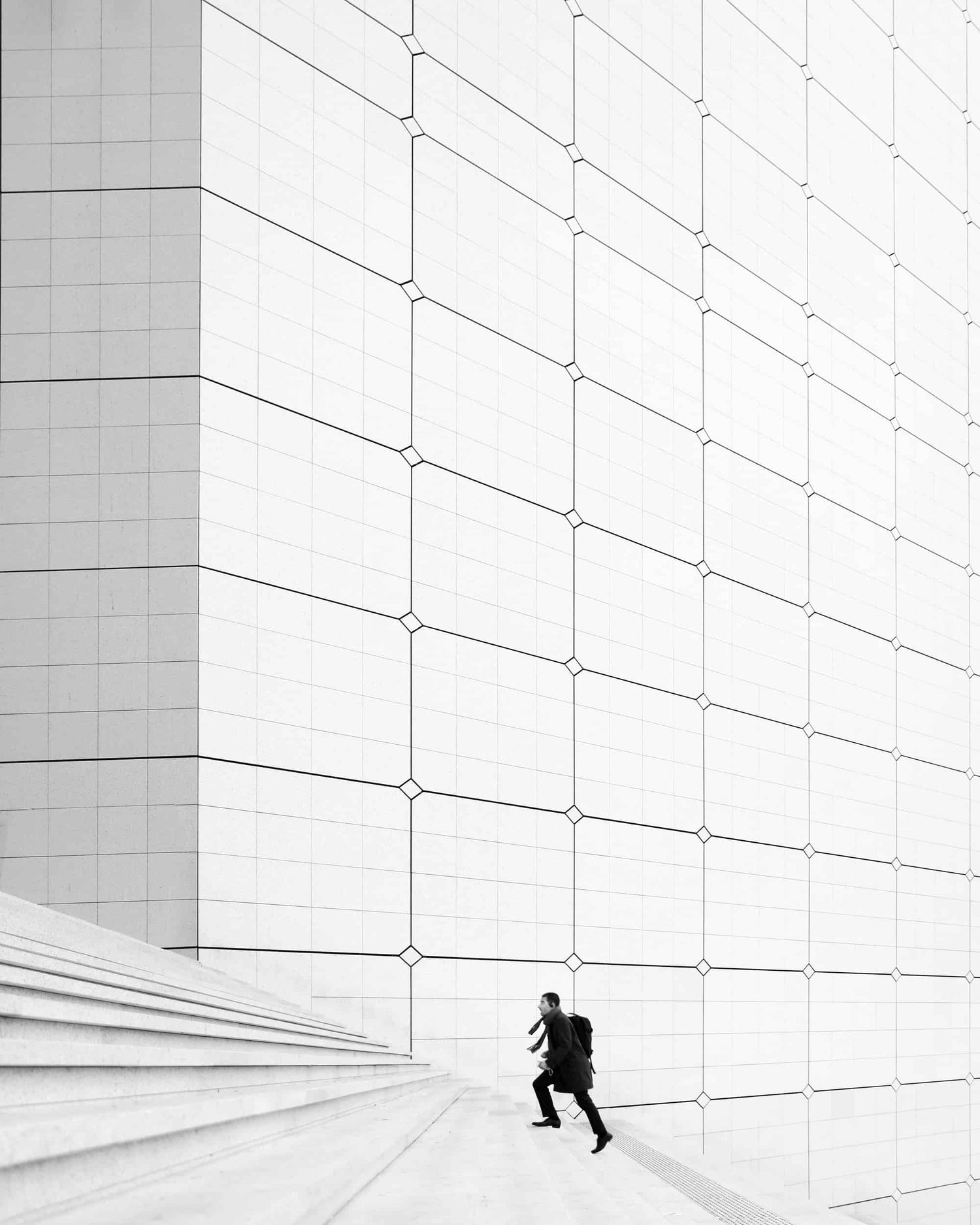 The artpiece 'Busy Business' by Nina Papiorek showing a single person running up otherwise empty steps in the business district La Défense in Paris. The artwork is completely in black and white.