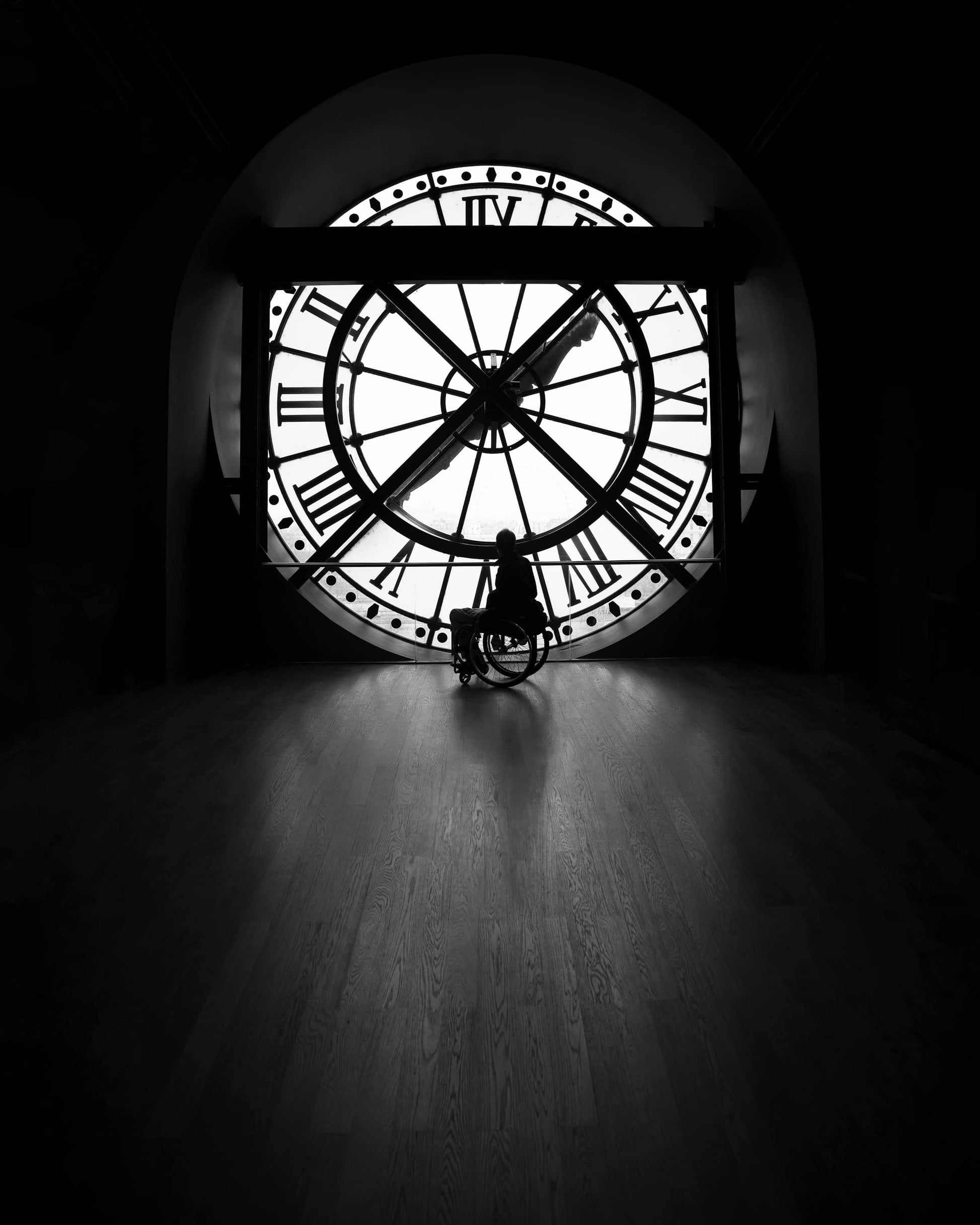 The artpiece 'Off a Free Spirit' by Nina Papiorek shows a single person in a wheelchair looking out of the clockwindow of the Musee D'Orsay. The artwork is completely in black and white.