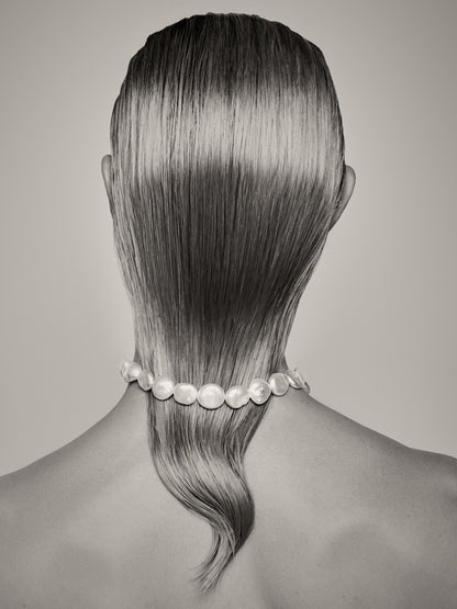 The artpiece 'Perfection' by Rebekka Eliza shows a person from behind, with their hair hanging over their back and a necklace around their neck and over their hair.