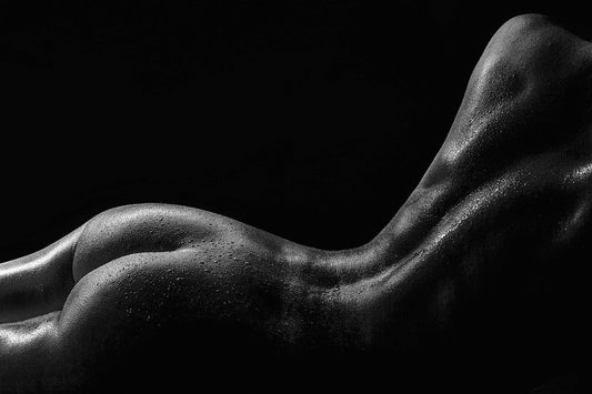 Side view of a woman laying on her chest, water droplets glistening on her back, set against a deep black background, captured by Ruslan Bolgov.