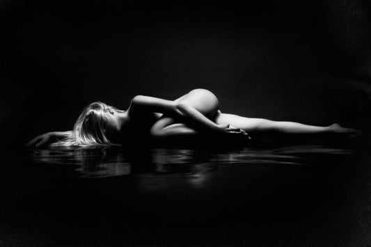 Woman laying on reflective fabric, her form intertwined with water ripples, illuminated from above, captured by Ruslan Bolgov.
