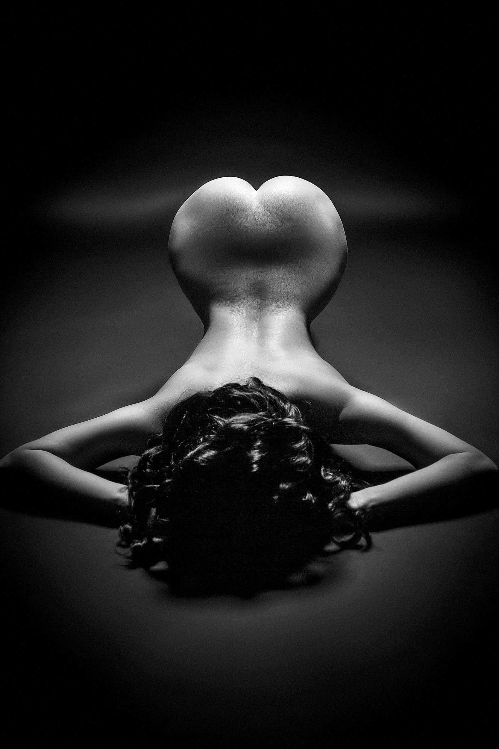 Woman laying on the floor, arms raised, back arched, accentuating the slim waist and wider thighs, captured in black and white by Ruslan Bolgov.