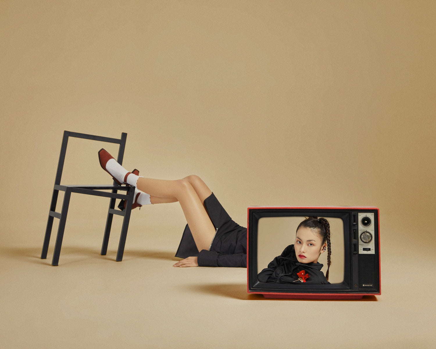 The artpiece 'Upside down' by Hui Long shows a woman laying on the floor next to a strangely deformed chair, with a tv blocking the womans face. The TV shows a strong and determined looking woman facing the camera.