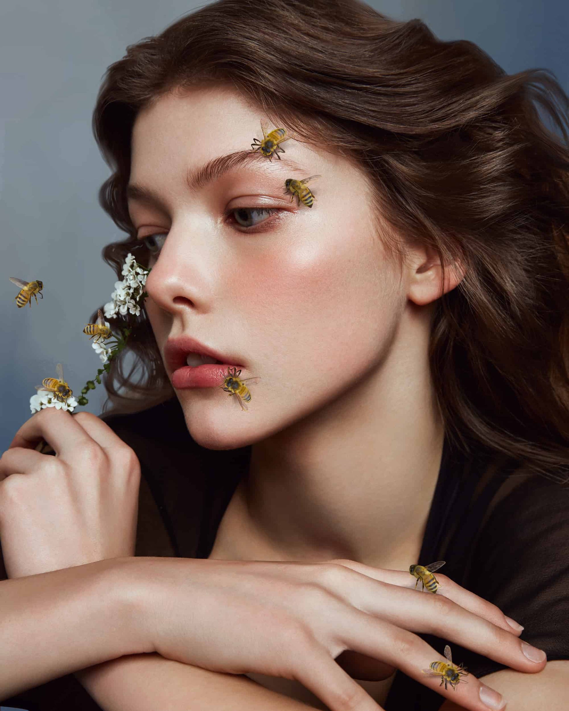 The artpiece 'Bee' by Yang Han from the series Blue Heart shows a brown haired woman, posing for a picture while there are bees, both flying around and sitting on her hands and face.